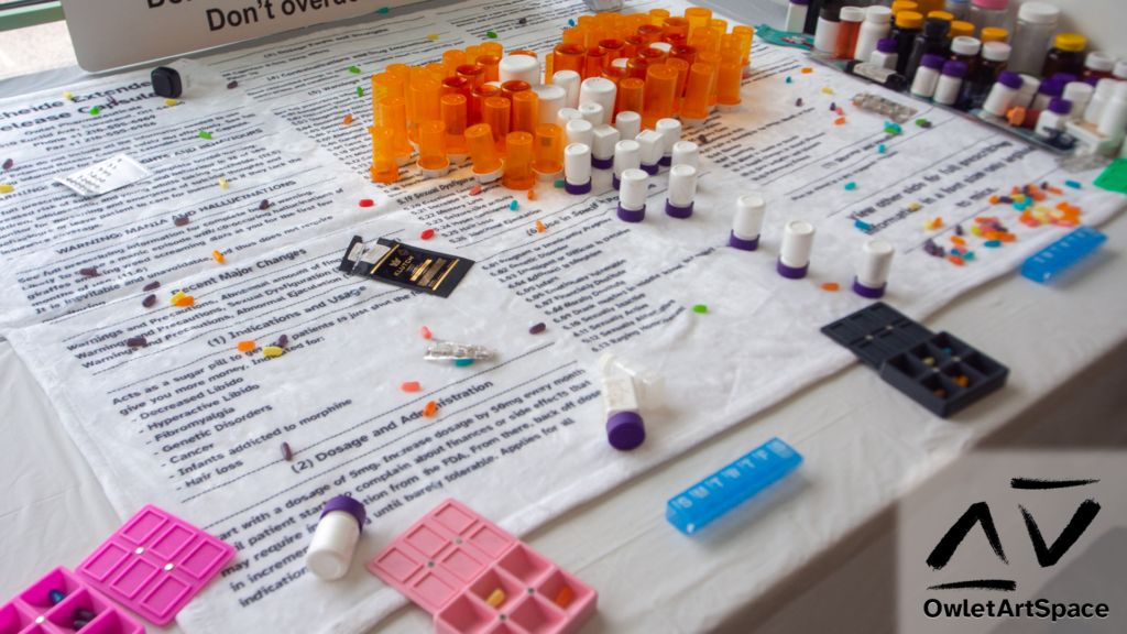A detailed shot showing the drooling mouth pill bottle mural, the intermingling of the loose candy representing pills on the medication warning blanket, and several of the medboxes containing those 'pills.'