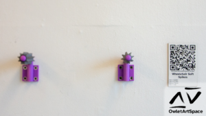 Two of the wheelchair soft spikes on purple mounts placed equidistant to our wheelchair handles. Next to it is a wall label with a QR code to the page you are currently reading.