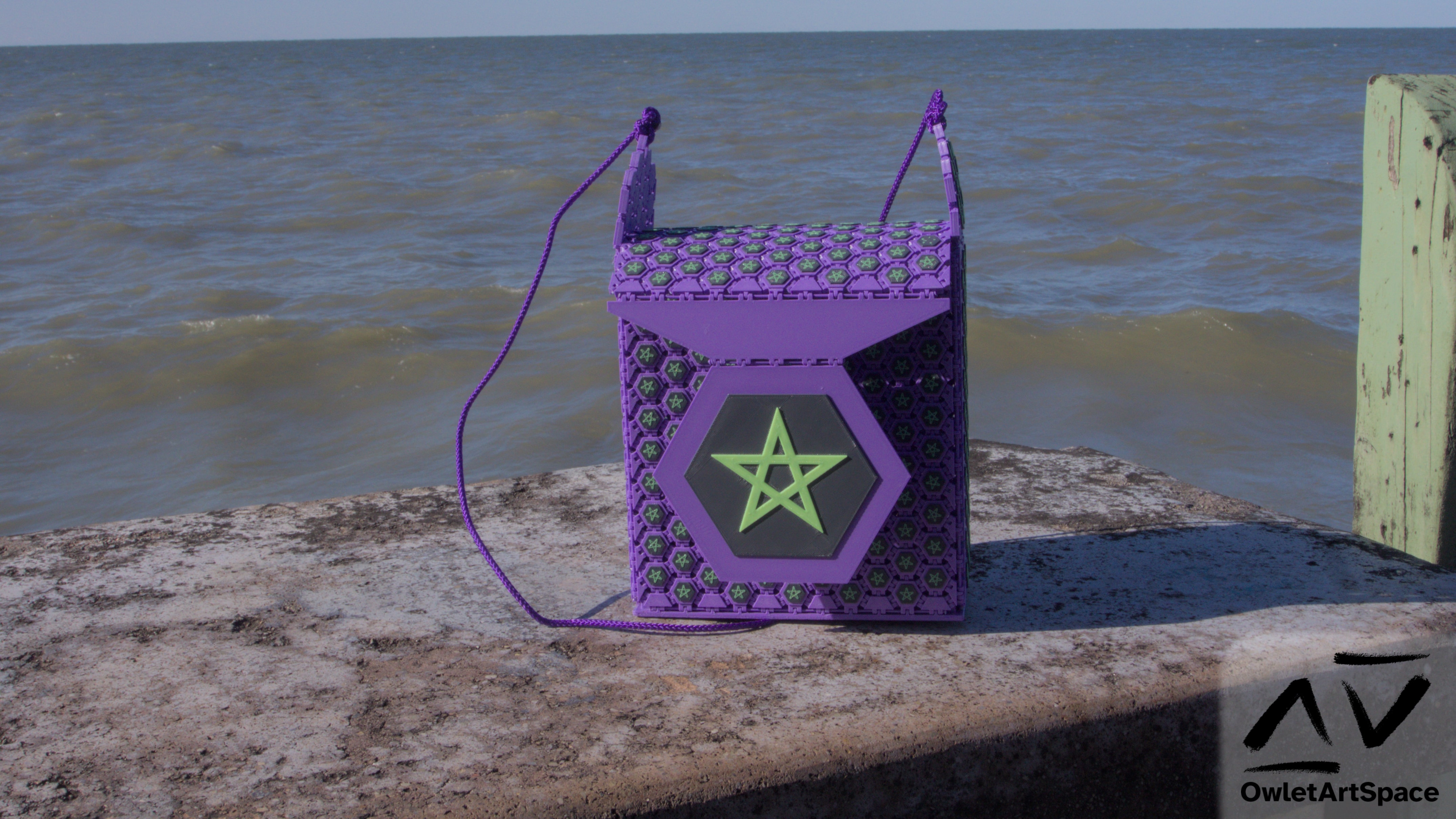 A purple purse made up of hexagonal pieces. The pieces have a smaller hexagon in gray with a yellow star in the center. The center flap is one of those segments made a lot larger. In the background, a lake.