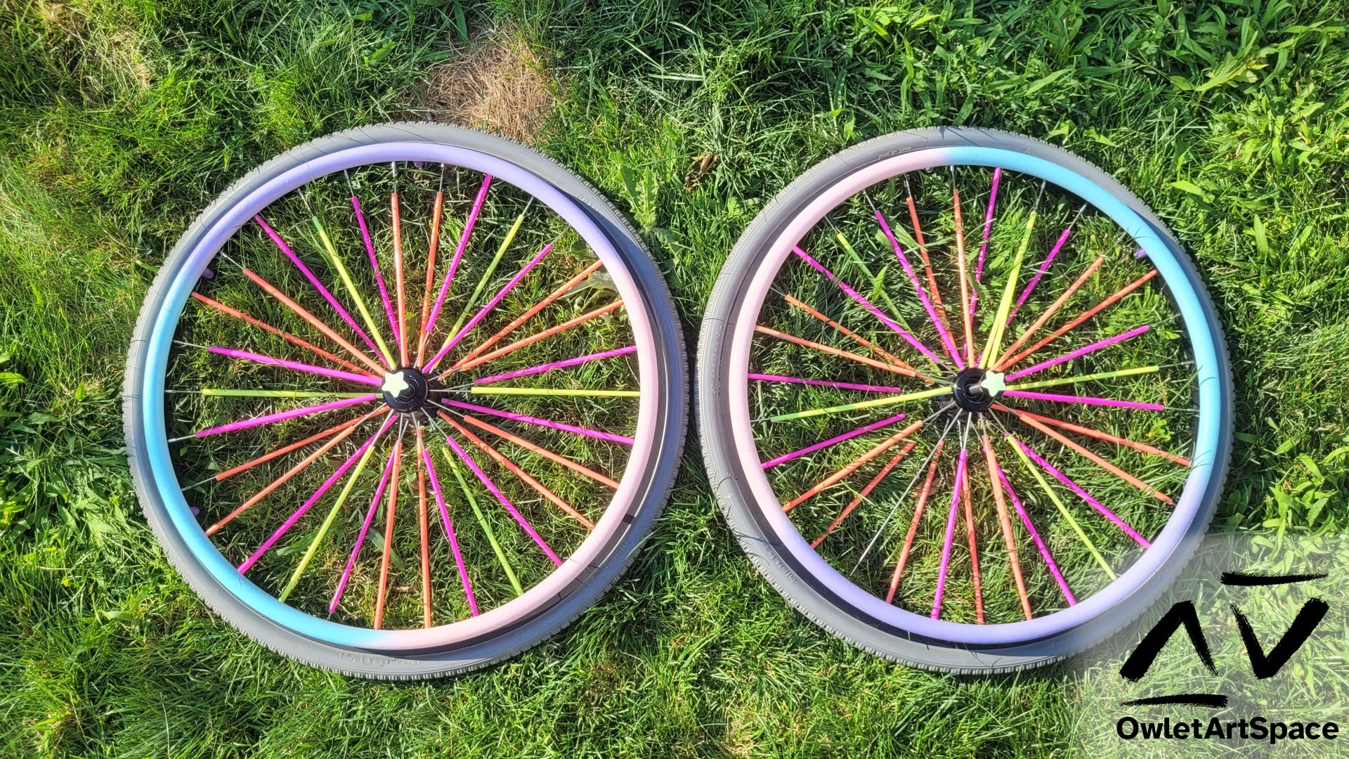 Two wheelchair wheels with fluorescent straws on the spokes, a glow in the dark star on the quick release axle, and a gradient between light pink, lavender, and light blue on the rim.